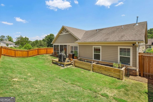 back of house with roof with shingles, a vegetable garden, a yard, a fenced backyard, and a sunroom