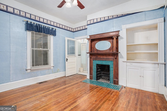 unfurnished living room featuring visible vents, a fireplace, a ceiling fan, and wood finished floors