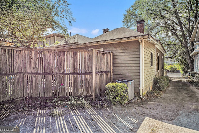 view of side of property with cooling unit, fence, and a chimney