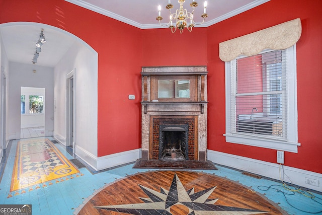 living room featuring a fireplace with raised hearth, track lighting, arched walkways, crown molding, and baseboards