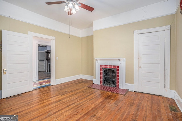 unfurnished living room with visible vents, a fireplace with raised hearth, a ceiling fan, wood finished floors, and baseboards