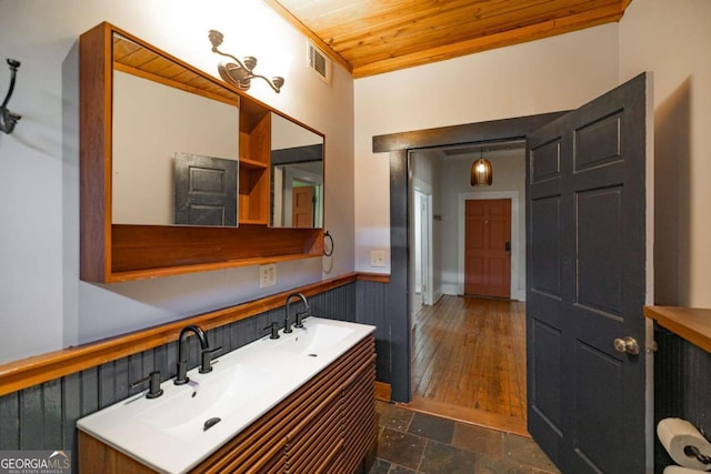 bathroom with stone tile floors, wood ceiling, wainscoting, and a sink