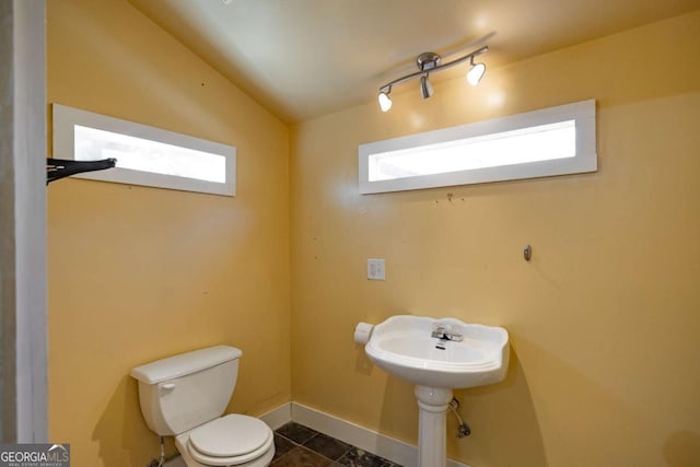 half bathroom featuring baseboards, toilet, tile patterned flooring, and vaulted ceiling