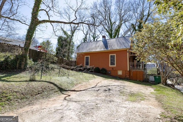 view of side of property featuring a chimney, metal roof, fence, and dirt driveway