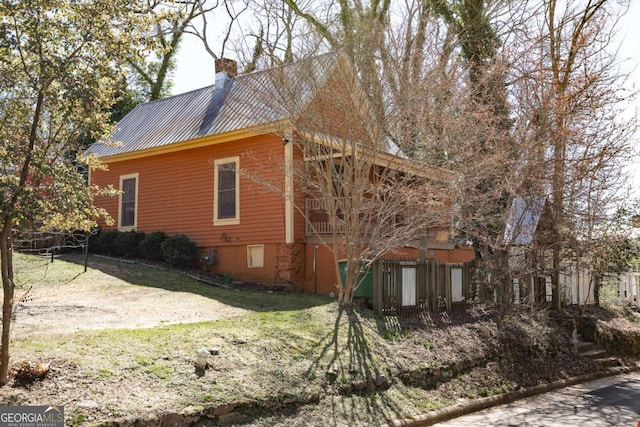 view of side of home with metal roof, a lawn, a chimney, and fence