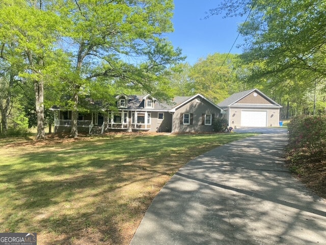 cape cod home with a front yard, a garage, covered porch, asphalt driveway, and an outbuilding