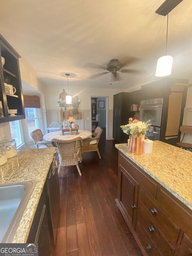 kitchen featuring dark wood-style flooring, light stone countertops, a sink, hanging light fixtures, and a ceiling fan