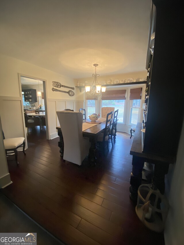 dining space featuring dark wood finished floors, a chandelier, and a wainscoted wall