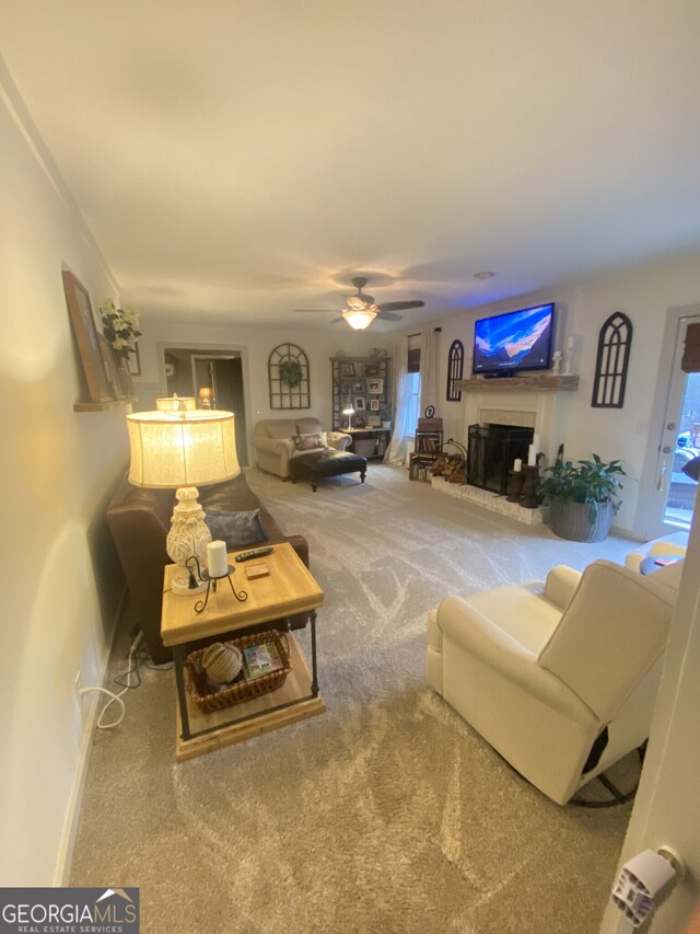 living area featuring carpet, a fireplace with raised hearth, ceiling fan, and baseboards