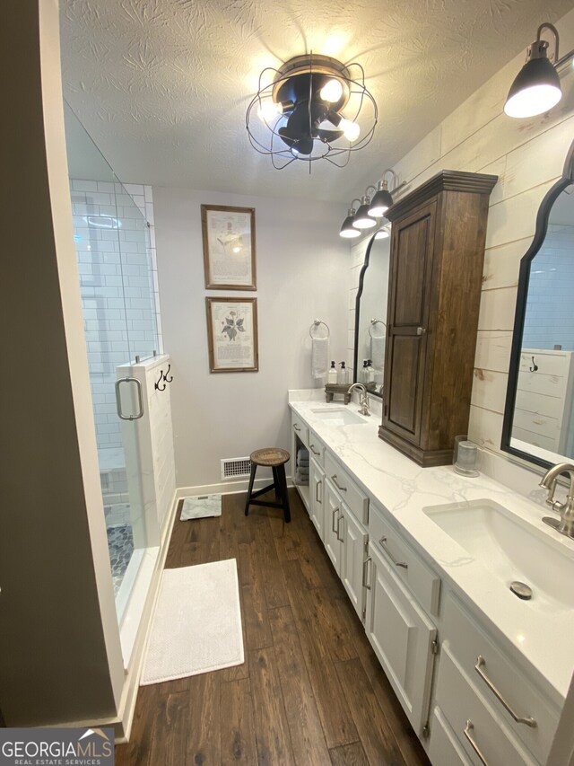 full bathroom featuring wood finished floors, a shower stall, a textured ceiling, and double vanity
