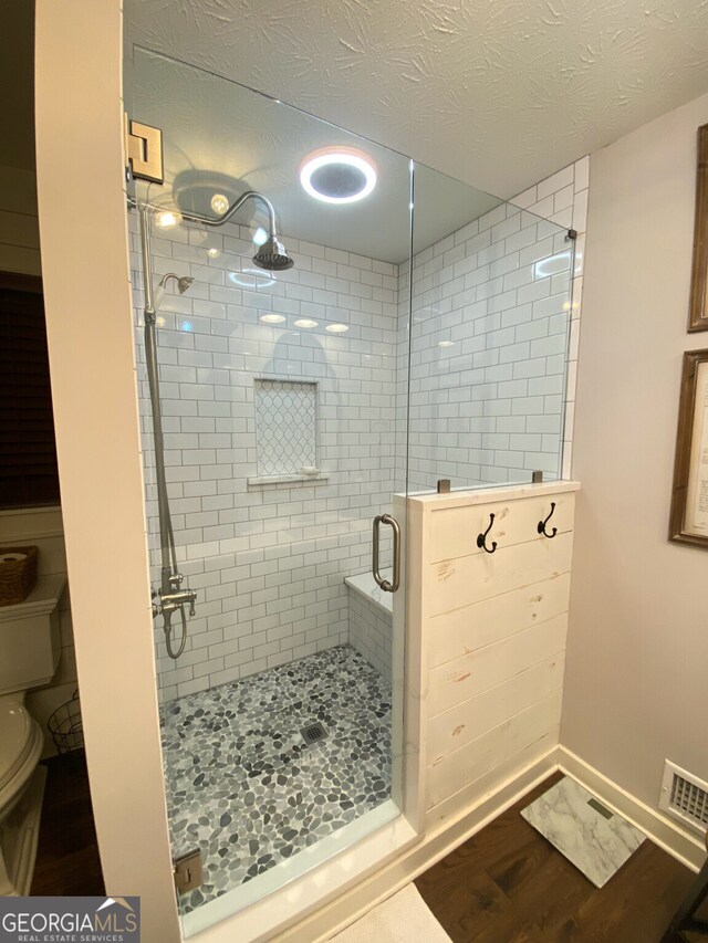 full bath with toilet, a shower stall, wood finished floors, and a textured ceiling