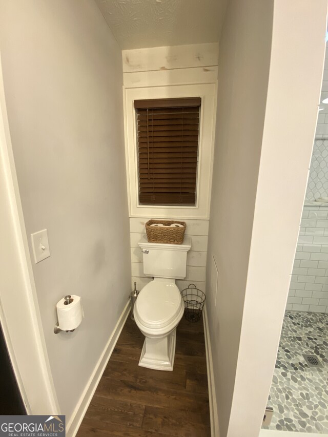 bathroom with a shower stall, toilet, wood finished floors, and baseboards