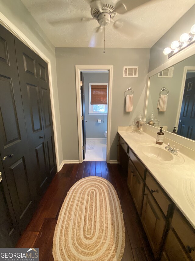 bathroom with wood finished floors, toilet, double vanity, a ceiling fan, and baseboards