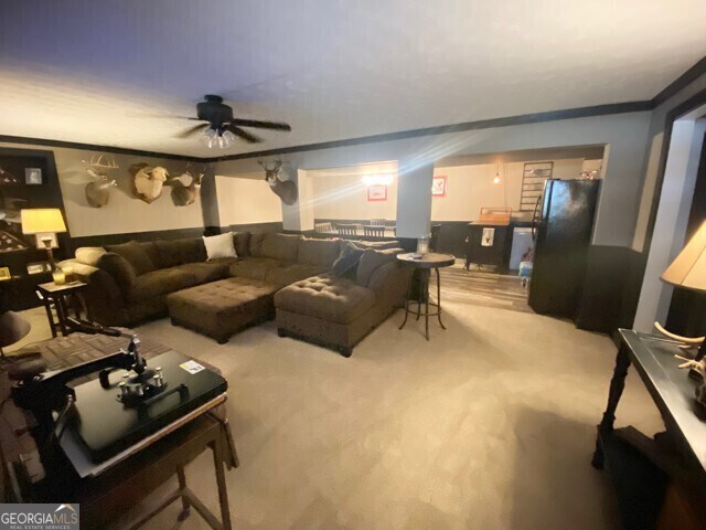 living room with ornamental molding, ceiling fan, and light carpet