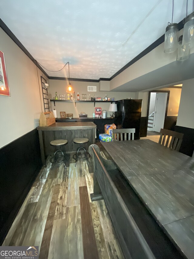 dining area featuring a dry bar, wood finished floors, and ornamental molding