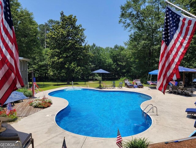 swimming pool with a patio area, a yard, and view of scattered trees