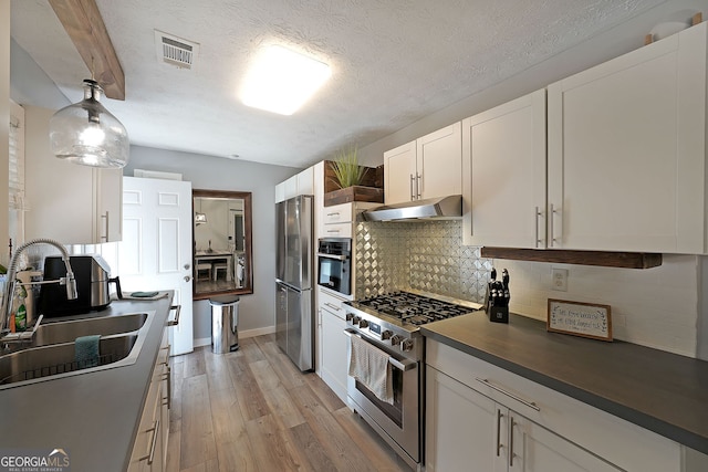 kitchen with under cabinet range hood, a sink, tasteful backsplash, dark countertops, and appliances with stainless steel finishes