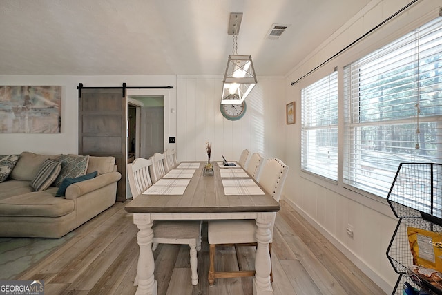 dining area with visible vents, light wood-style floors, and a barn door