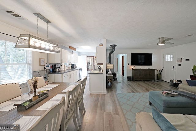 dining area featuring light wood-type flooring, visible vents, a textured ceiling, and ceiling fan