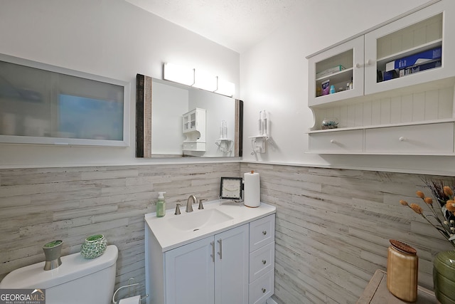 half bath featuring vanity, tile walls, toilet, and a wainscoted wall