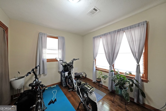 workout room with visible vents, baseboards, a textured ceiling, and wood finished floors