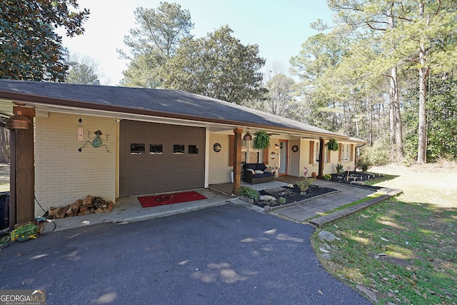 ranch-style home featuring brick siding, covered porch, driveway, and a garage