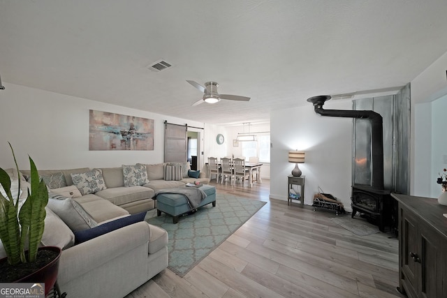 living room featuring visible vents, ceiling fan, a barn door, a wood stove, and light wood-style floors