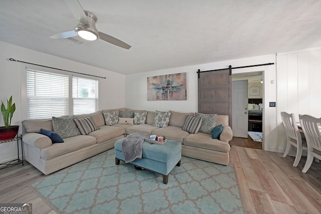 living area featuring a barn door, a ceiling fan, light wood-type flooring, and a textured ceiling