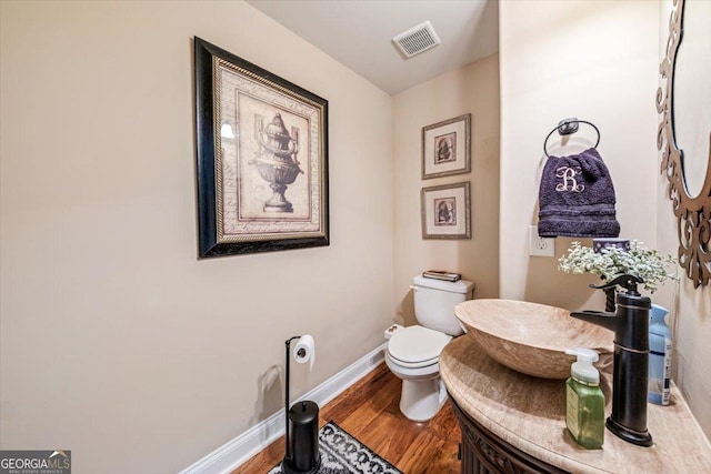 half bath featuring visible vents, baseboards, toilet, and wood finished floors