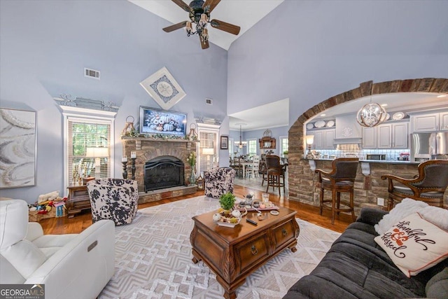 living area with visible vents, ceiling fan with notable chandelier, a stone fireplace, and light wood finished floors