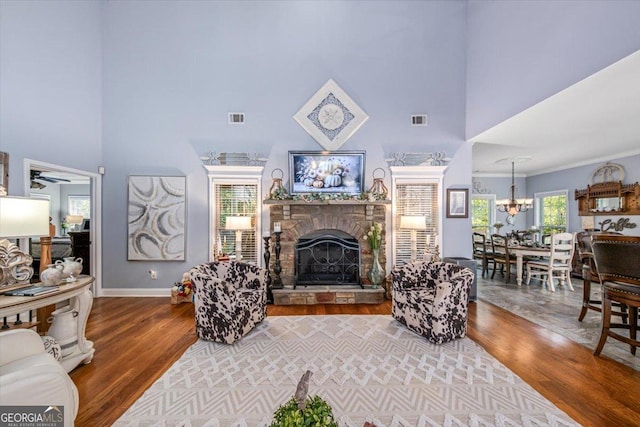 living room with wood finished floors, visible vents, baseboards, a fireplace, and a towering ceiling