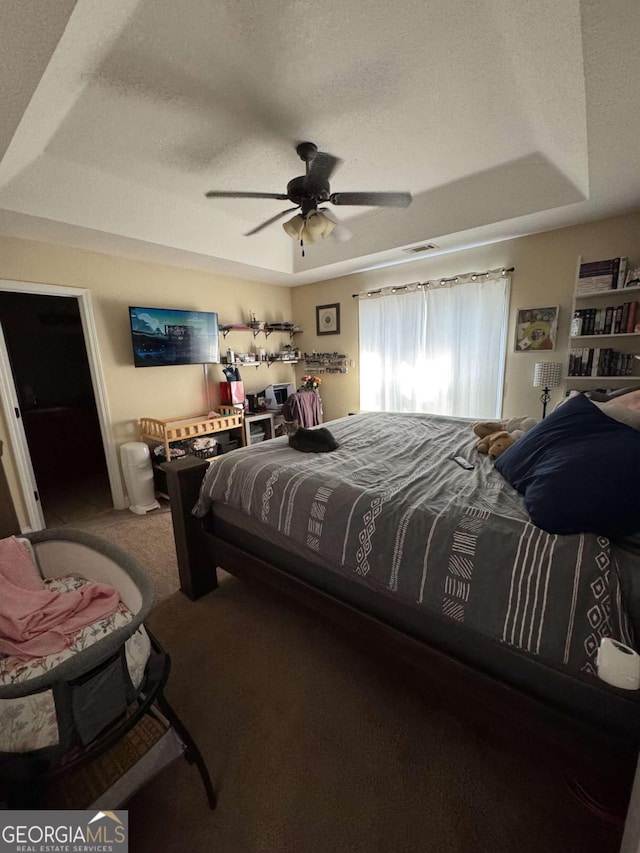 bedroom with a tray ceiling, carpet flooring, a ceiling fan, and a textured ceiling