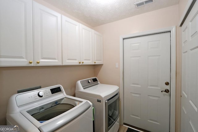 laundry area featuring separate washer and dryer, cabinet space, visible vents, and a textured ceiling