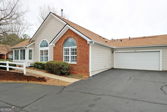 view of front of home with brick siding, a shingled roof, fence, aphalt driveway, and a garage