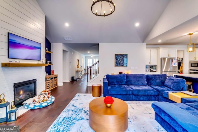 living room featuring dark wood-style floors, recessed lighting, lofted ceiling, a brick fireplace, and stairs