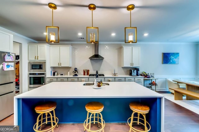 kitchen featuring ornamental molding, a kitchen breakfast bar, stainless steel appliances, wall chimney exhaust hood, and a sink