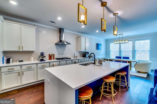 kitchen with gas cooktop, wall chimney range hood, crown molding, and a sink