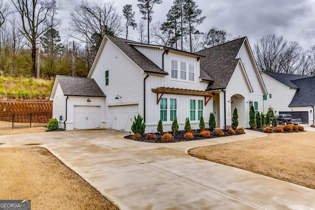 modern inspired farmhouse featuring fence, roof with shingles, an attached garage, concrete driveway, and board and batten siding