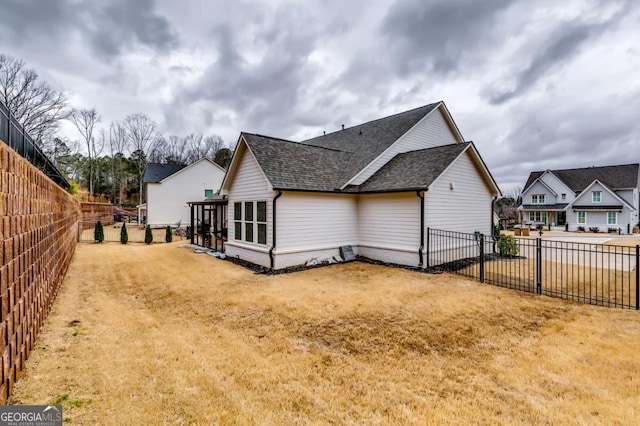 view of property exterior featuring a yard, a fenced backyard, and a shingled roof