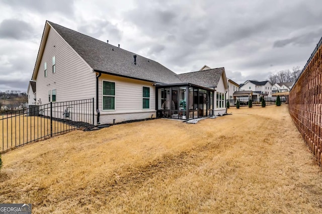 rear view of house featuring a yard, a shingled roof, a fenced backyard, and a sunroom