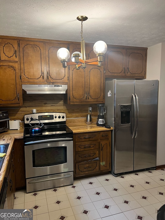 kitchen with an inviting chandelier, under cabinet range hood, light countertops, and appliances with stainless steel finishes