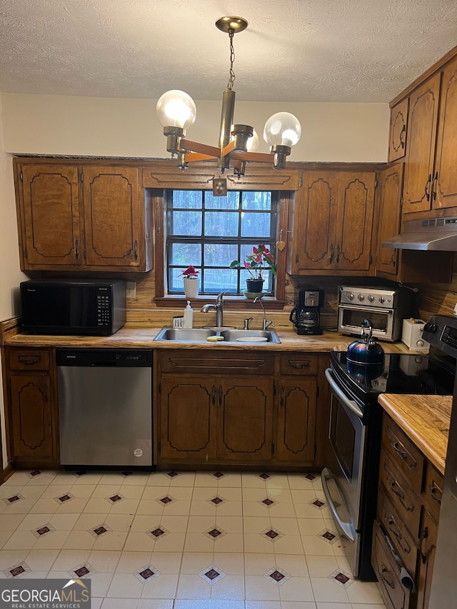 kitchen with under cabinet range hood, a sink, stainless steel appliances, an inviting chandelier, and light countertops