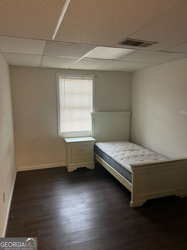 unfurnished bedroom with dark wood-style floors, visible vents, baseboards, and a drop ceiling