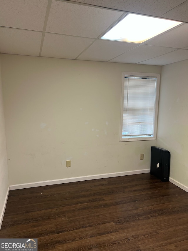 empty room featuring a paneled ceiling, baseboards, and dark wood-style flooring