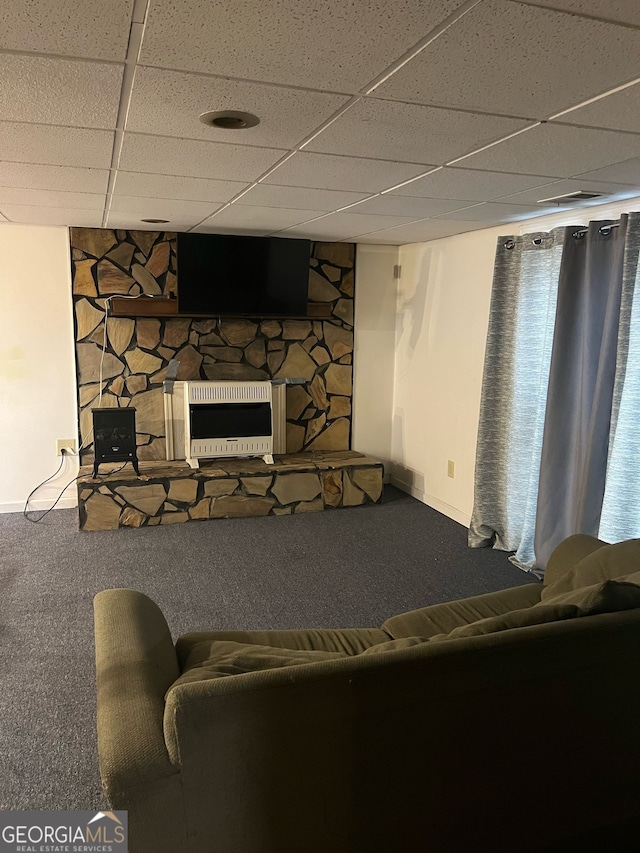 carpeted living room featuring heating unit, a stone fireplace, and a drop ceiling