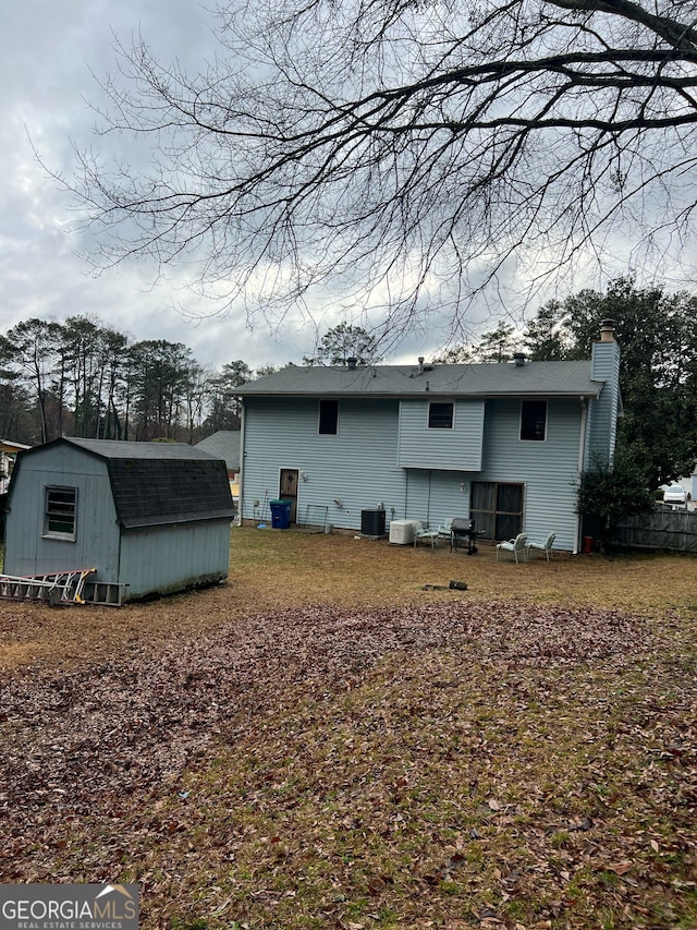 back of house with an outbuilding, central AC unit, a chimney, and a storage shed