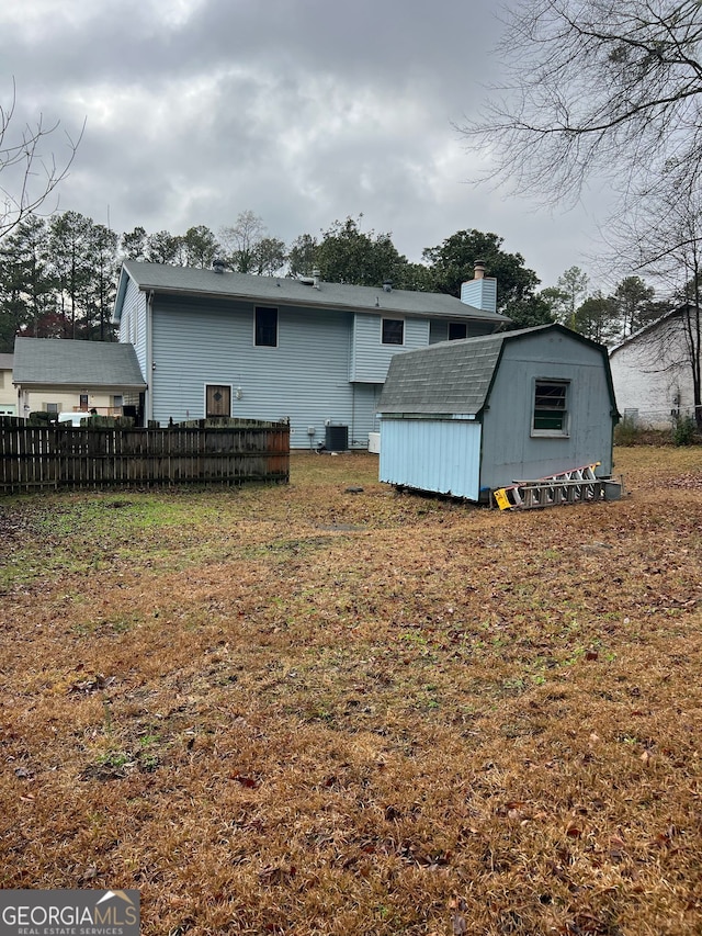 back of property with an outbuilding, cooling unit, fence, a chimney, and a storage shed