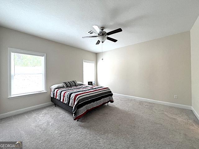 carpeted bedroom with visible vents, baseboards, a textured ceiling, and a ceiling fan