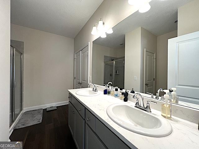 bathroom featuring a sink, baseboards, wood finished floors, and a shower stall