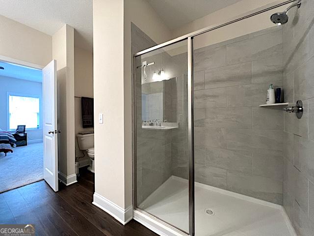 bathroom featuring toilet, wood finished floors, a stall shower, and baseboards